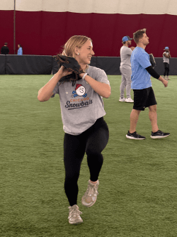 A player in a Snowballs shirt and glove steps into a throw during warm-ups on the turf