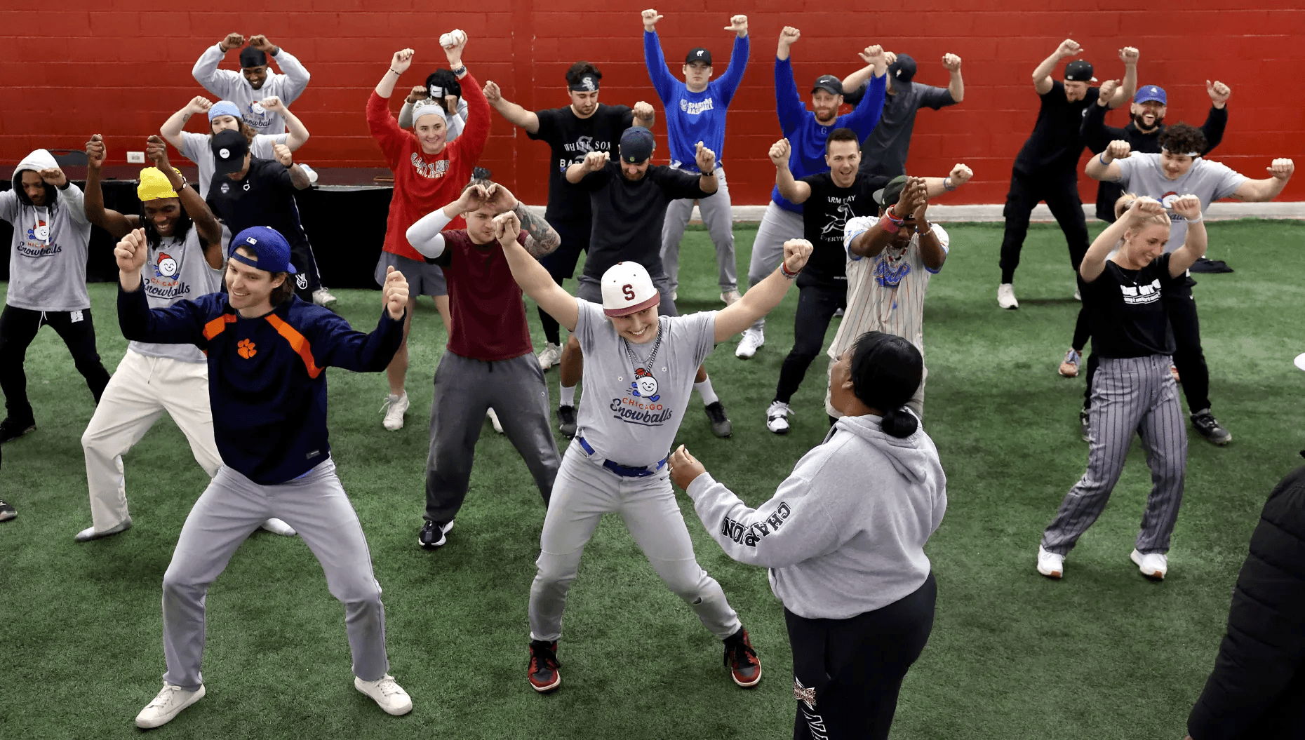 Dozens of players spread across an indoor turf field, arms raised mid-routine, following a choreographer in the foreground